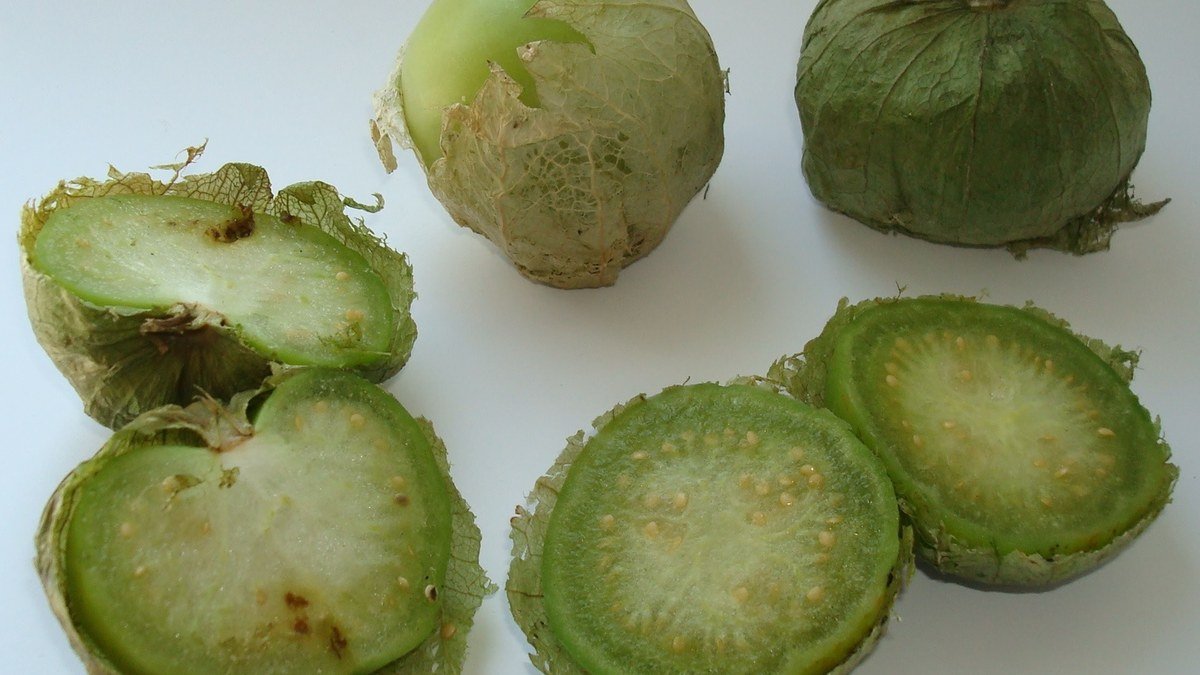 Real tomatillos shown inside papery husks and cut open to reveal the green fruit and seeds