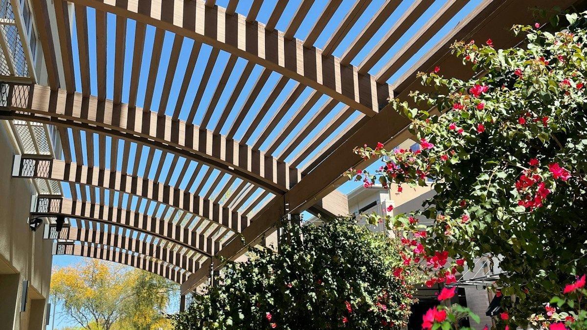 A covered patio walkway with striped shade and flowering container plants